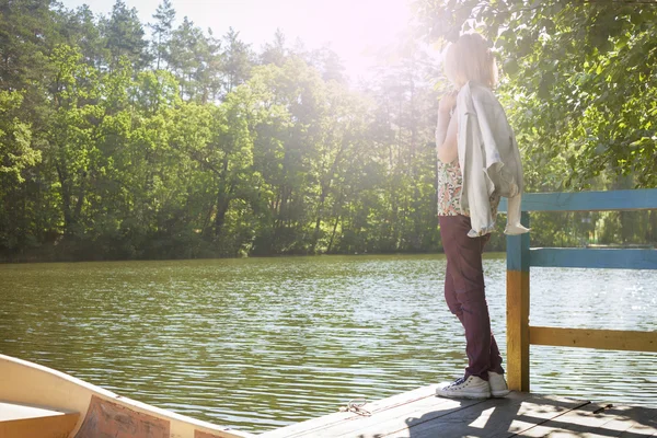 Young woman fashion leisure on the lake during a vacation in the woods girl sitting. View from the back