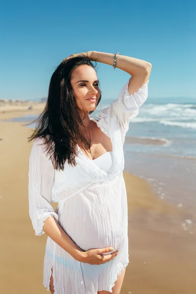 Future young mother in a white dress on the beach