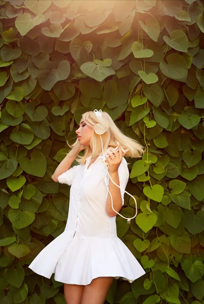 Blonde woman dancing in a green leaves while listening to music