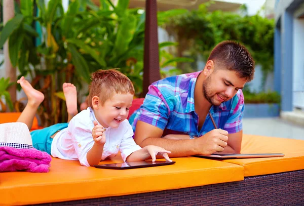 Happy father and son busy with digital tablet on vacation