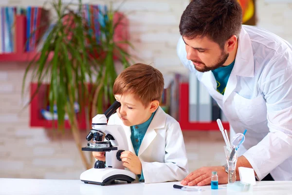 Teacher helps kid to conduct experiment with microscope in school lab