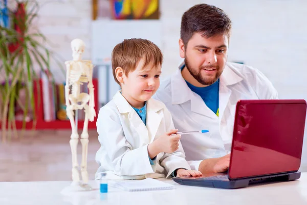 Teacher explains a human body structure to little pupil with the help of laptop