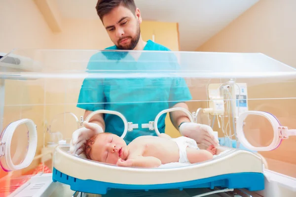 Medical staff taking care of newborn baby in infant incubator