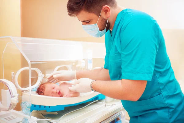 Medical staff taking care of newborn baby in infant incubator