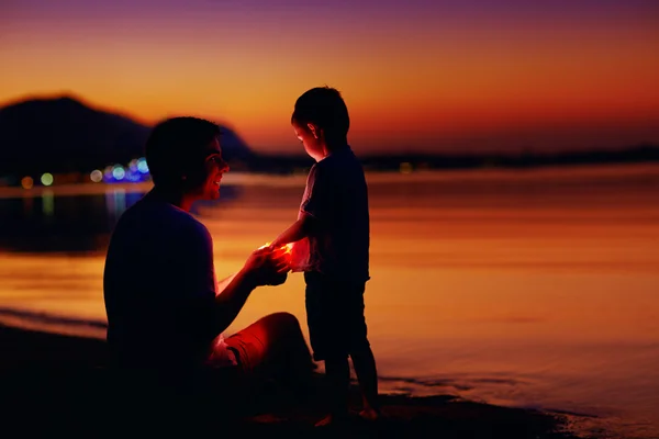 Happy father and son with lantern at sunset beach