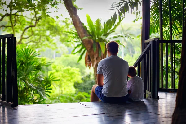 Father and son sitting on tree house stairs in tropical forest