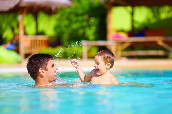 Joyful father and son having fun in pool, summer holidays