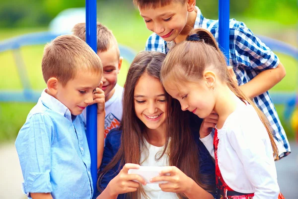 Group of happy kids playing online games together, outdoors