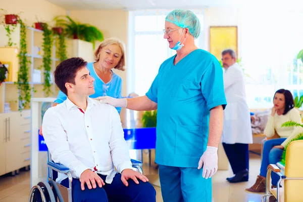 Surgeon and medical staff talking with young adult man in wheelchair, in hospital