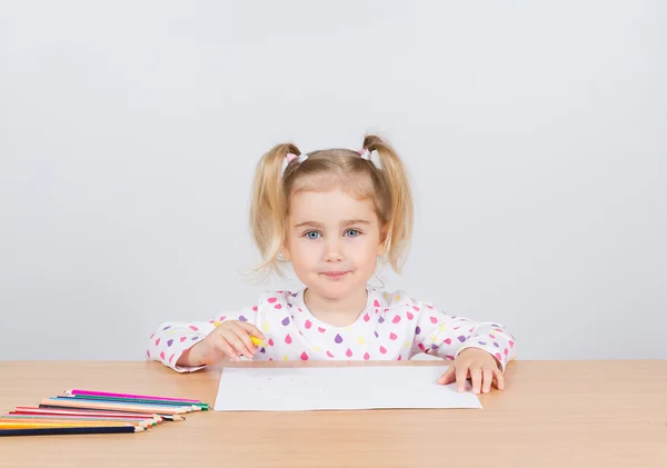 Little girl draws at table pencils.