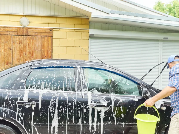 Man washing his black car near house.