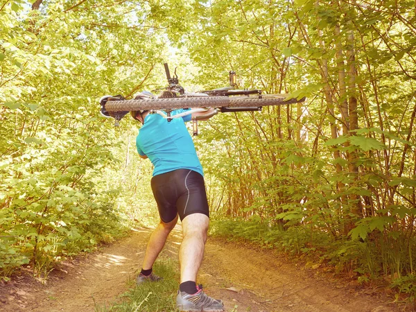 Cyclist man carries bicycle in green forest in summer.