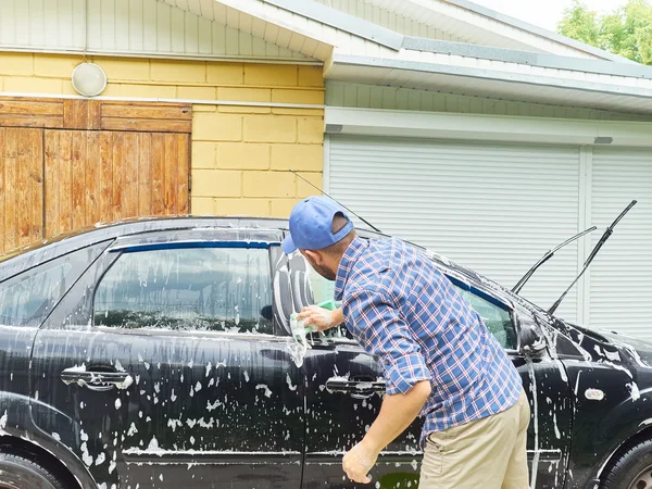 Man washing his black car near house.