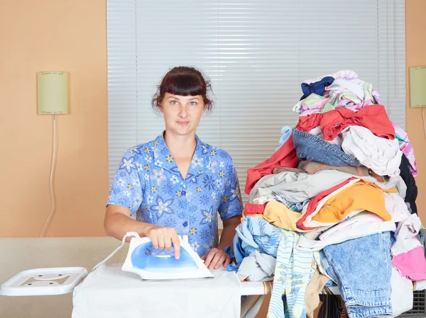 Young Caucasian woman ironed clothes in the room near  window.