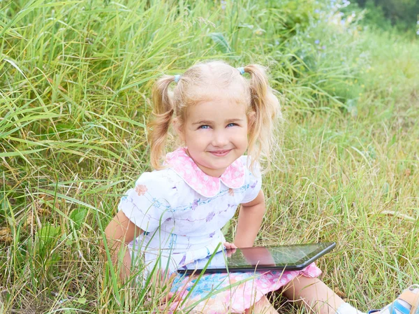 Little girl sitting in park on sunny day and play with tablet pc
