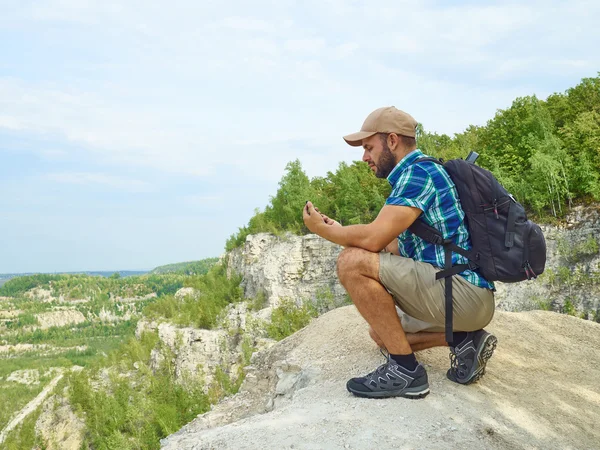 Man tourist is using a smartphone while sitting on the edge of a
