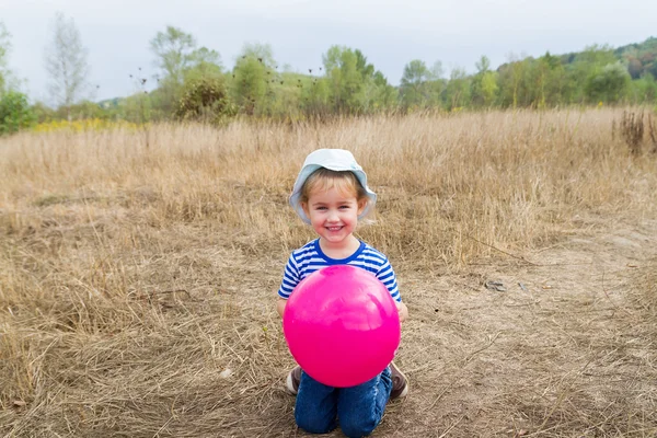 A little girl is sitting with a pink ball