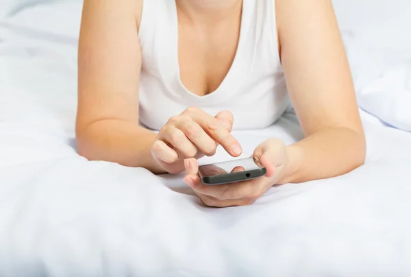 Young caucasian woman on the bed with smartphone