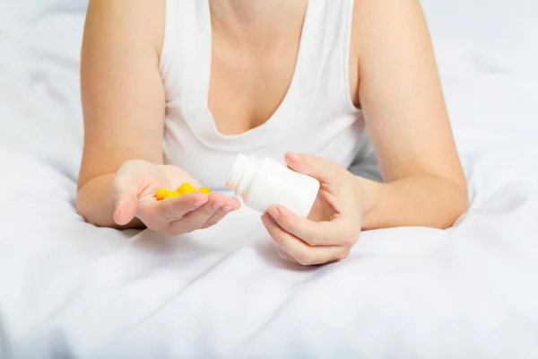Woman in her pajamas in bed holding yellow pills