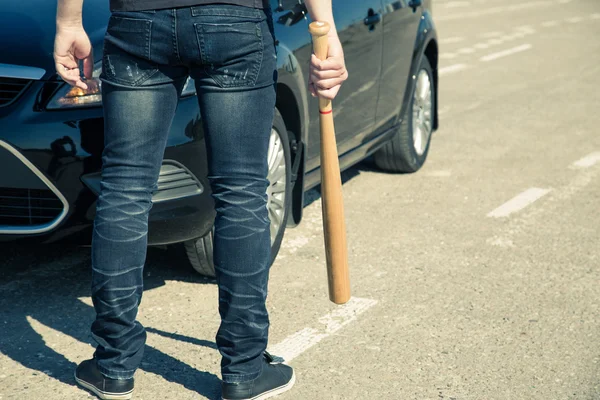 Man with baseball bat on the road before the car