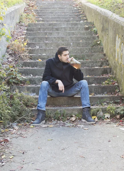 Young man drinking alcohol outdoor on concrete stairways
