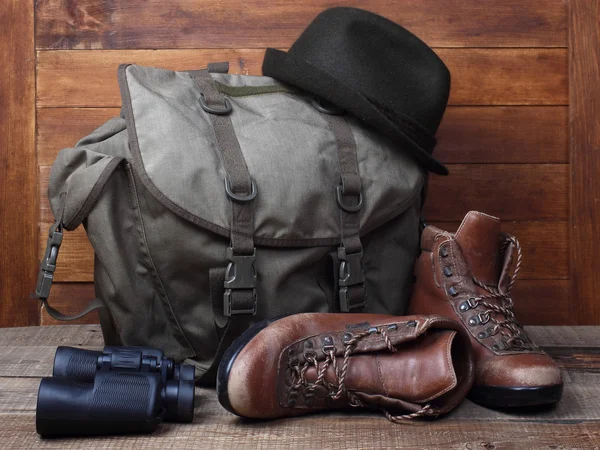 Rucksack with old boots, binocular and hat on wooden background