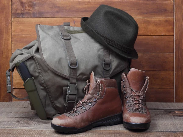 Rucksack with old boots, knife and hat on wooden background