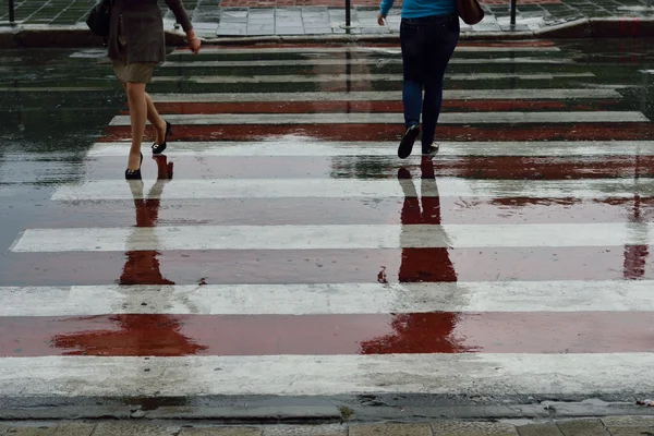 Reflections of people crossing the road in puddles
