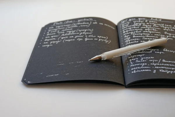 Notebook with black paper and white pen opened with page and white on black text