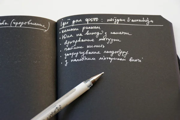 Notebook with black paper and white pen opened with page and white on black text