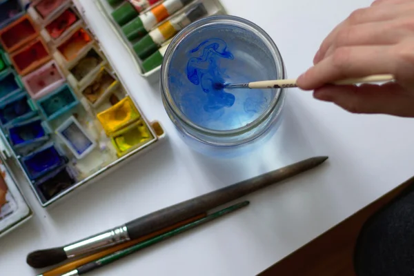 Drawing with watercolor paint and puting down brush into the water