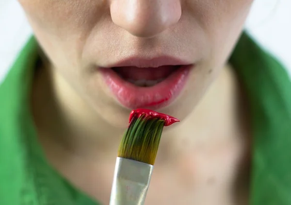 Girl artist putting brush with paint close to her lips