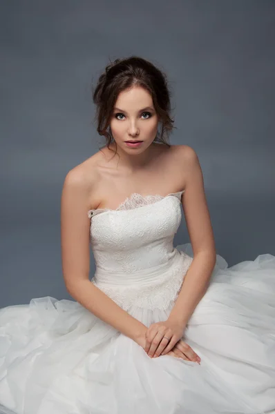 Adorable young bride with brown curly hair sitting in a cloud of