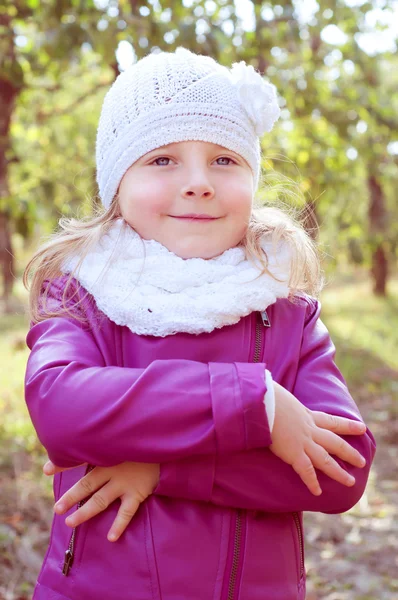 Cute little blond girl in a white knitted hat and scarf. Fall la
