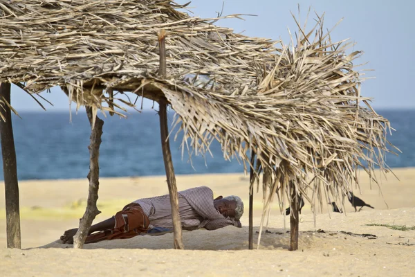 Old man resting in shadow in Sri Lanka beach