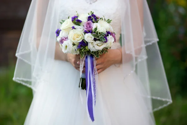 Young beautiful Bride holding bouquet of purple, violet, yellow, and cream-colored roses,  other flowers mixed with wild greens.