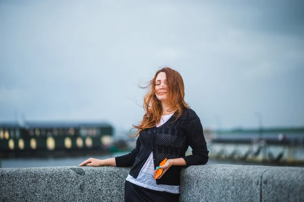 Brown haired girl with closed eyes and flying hair on wind standing at river bank. Concept of a cold, windy weather, loneliness