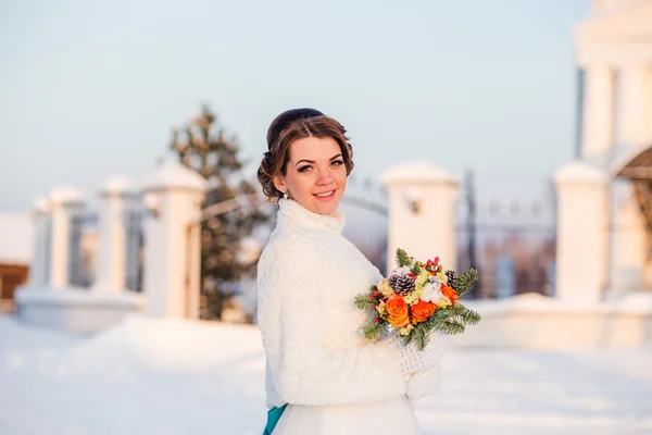 Happy beautiful bride smiles and holds bouquet of orange roses at winter outdoors