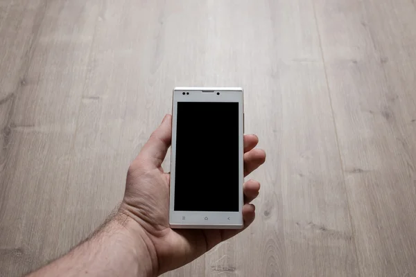 Close up of a white mans hands using white smartphone with blank black screen. Wood background