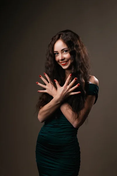 Brunette girl  with curly long hair shows beautiful hands with long fingers and fashionable design of healthful red nails on dark  background
