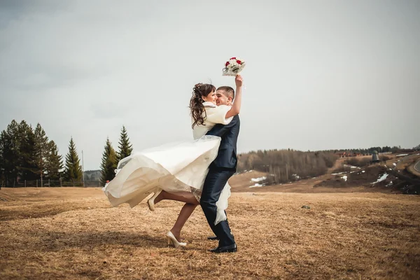 Wedding  couple embracing on open spaces at winter The groom lifts the happy bride with bouquet