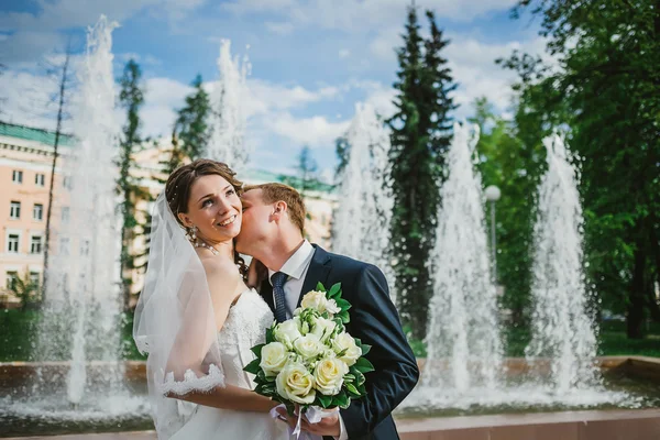 The groom and the bride kissing near a fountain