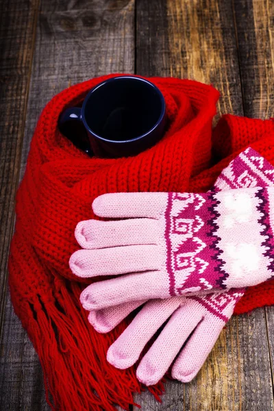 Cup of hot drink wrapped by red scarf and gloves on wooden board