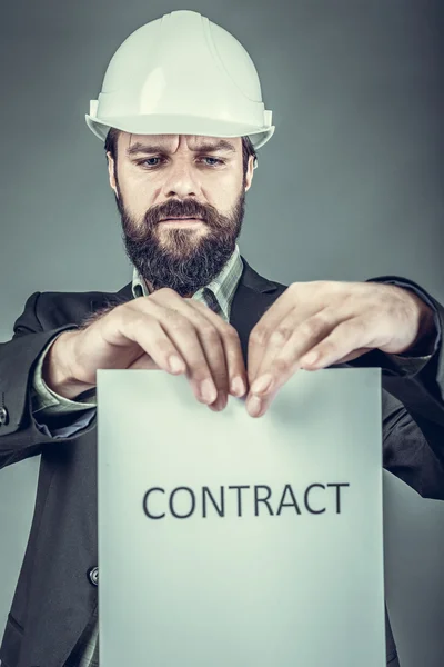 Frustrated young engineer with hardhat  tearing apart a contract