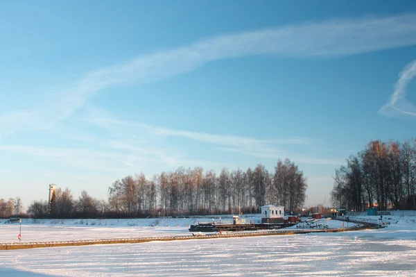 Striped landscape - ice on the river, boat station and blue sky