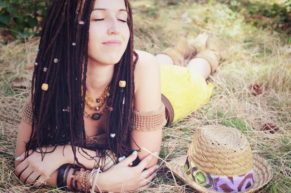 Relaxed and calm indie style woman with dreadlocks hairstyle, lying and resting in the dry grass,
