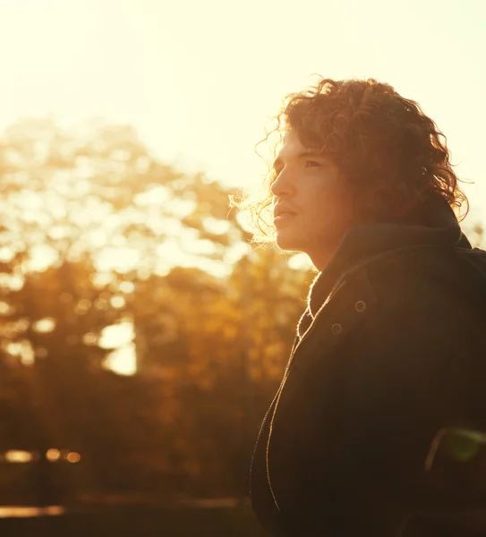 Young man with curly hair portrait in autumn park at a sunset.