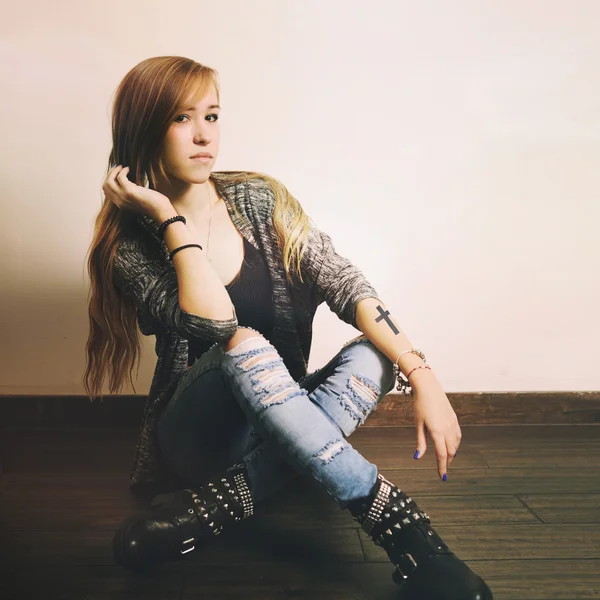 Young caucasian woman with cross tattoo on a hand sitting on a floor.