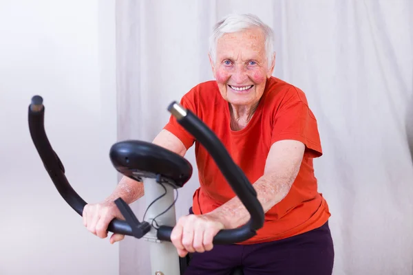 Happy elderly woman spinning on indoor stationary bicycle