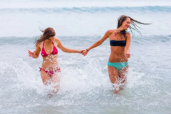 Women running in the water holding hands